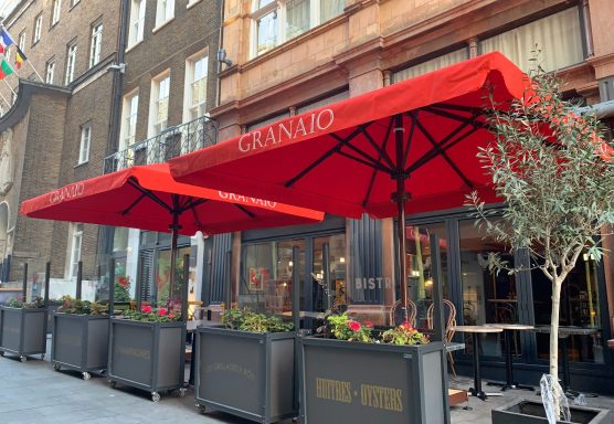 Red awnings over outdoor seating with plants outside a restaurant.