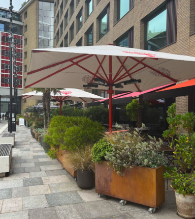 Outdoor seating area with umbrellas and planters in a modern urban setting.