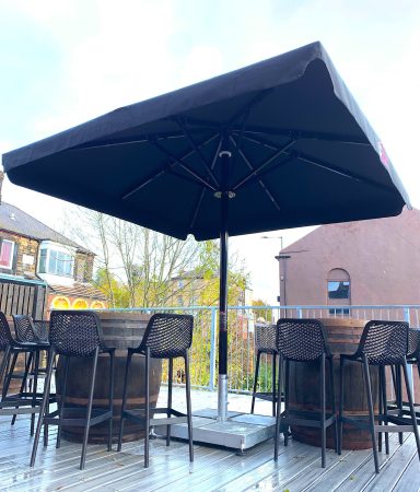 Outdoor seating area with a large umbrella and barrel tables on a wooden deck.