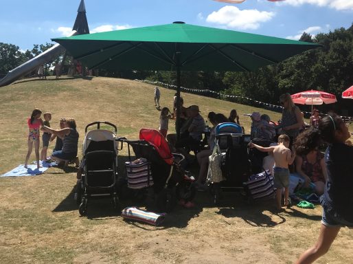 Group of people, including children, enjoying a sunny day under a large green umbrella.