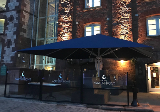 Outdoor dining area with a large blue umbrella in front of a brick building at night.