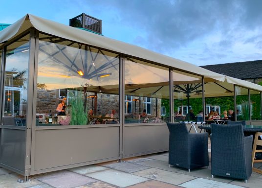 Outdoor dining area with a canopy, tables, and chairs under a cloudy sky.