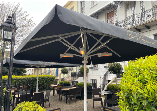 Outdoor dining area with black umbrellas and greenery in a restaurant setting.