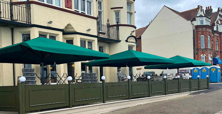 Outdoor seating area with green umbrellas and enclosed fencing outside a building.