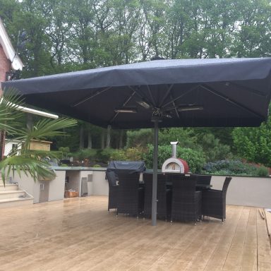 Outdoor patio area with a large black umbrella and wicker furniture surrounded by greenery.