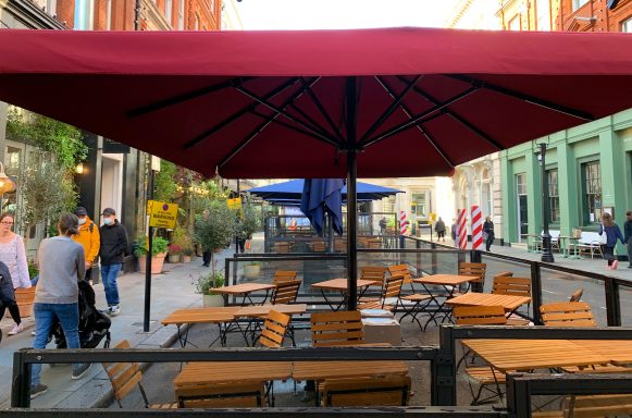 Outdoor café seating under a maroon umbrella in a lively street.