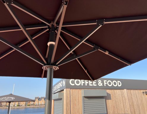 View of a brown parasol with a coffee and food stand in the background.