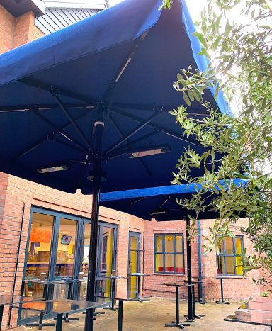 Blue canopies provide shade over outdoor seating area by a building.