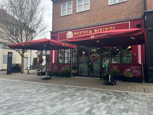 Red awning café with outdoor seating, set in a brick building on a paved street.