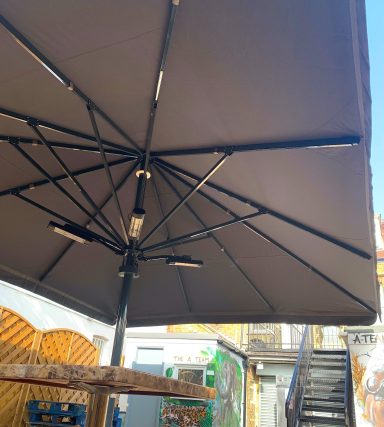 A large brown patio umbrella with a black frame, set against a blurred background.