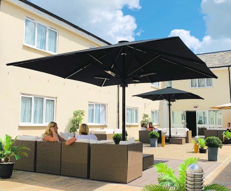 Outdoor seating area with umbrellas, plants, and two people relaxing.