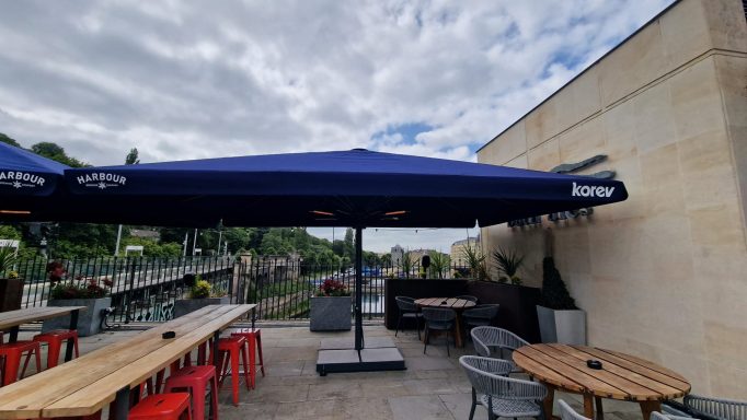 Outdoor dining area with blue umbrellas, wooden tables, and red chairs.