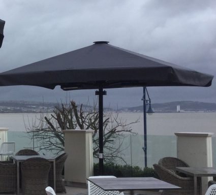 A large black parasol overlooks a cloudy waterfront with distant structures.