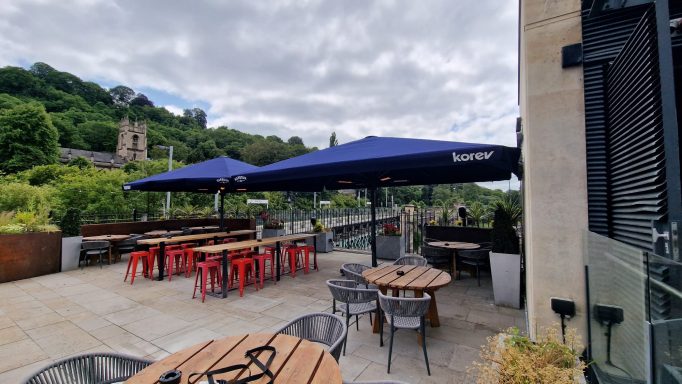 Outdoor seating area with wooden tables, chairs, and large blue umbrellas.