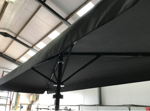 Close-up of a black fabric umbrella canopy and its supporting structure indoors.