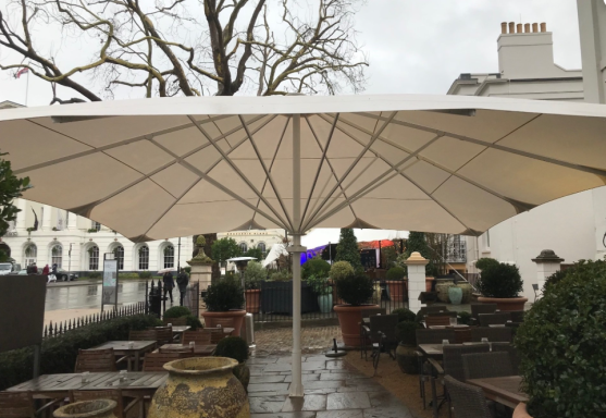 A large white umbrella provides shade over a patio with plants and seating.