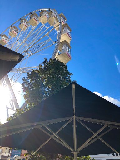 A Ferris wheel against a blue sky, partially obscured by a shaded umbrella.