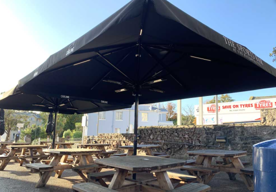 Outdoor seating area with wooden tables under a large black canopy.