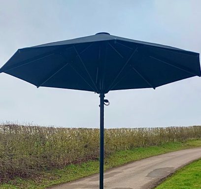 Black parasol on a path beside grassy fields under a cloudy sky.