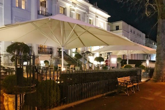 Outdoor seating area with large umbrellas, illuminated at night near a building.