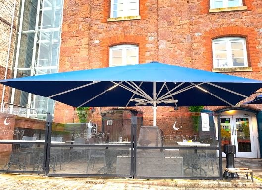 Blue parasol over outdoor seating area against a brick building.