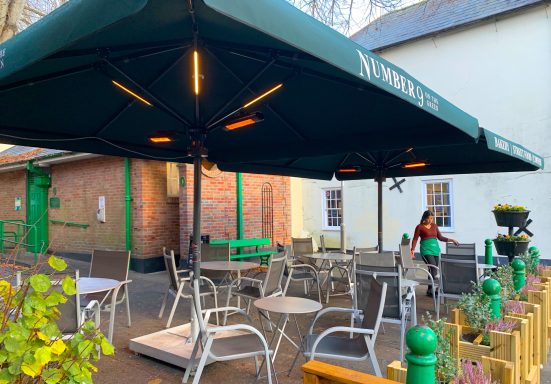 Outdoor seating area with green parasol, tables, and a person arranging chairs.