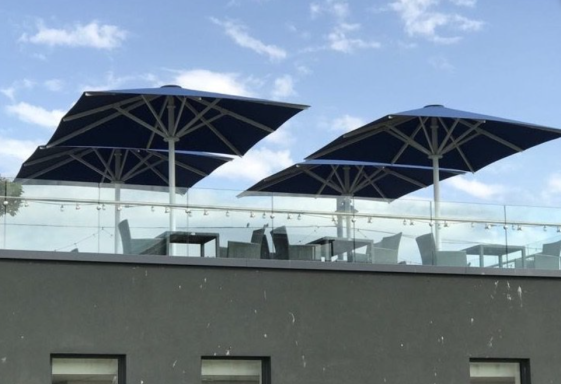 Two large blue umbrellas positioned over a rooftop terrace with seating.