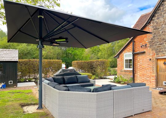 A garden seating area with a large black parasol and cushioned sectional sofa.