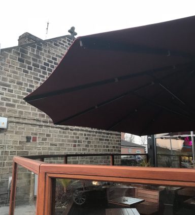 Brown parasol extending over a wooden seating area outside a building.