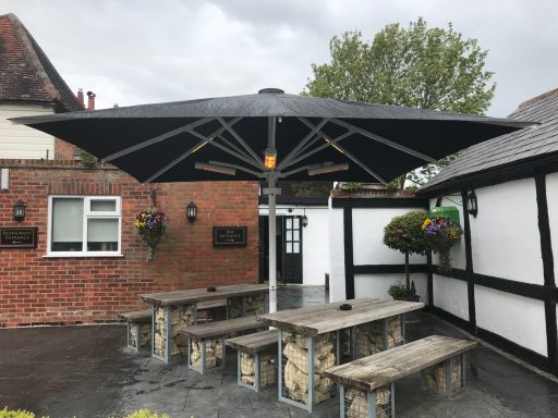 Outdoor seating area with large black parasol and stone benches near a building.