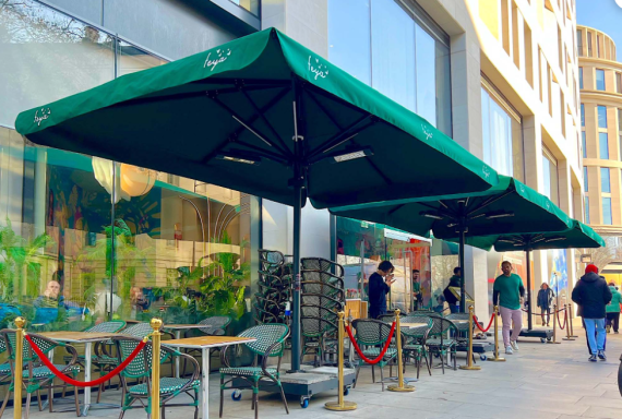 Outdoor café with green umbrellas and tables along a city street.