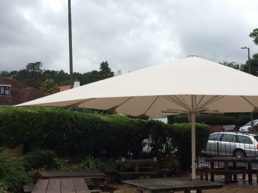 A large, white outdoor umbrella shading wooden picnic tables in a garden setting.